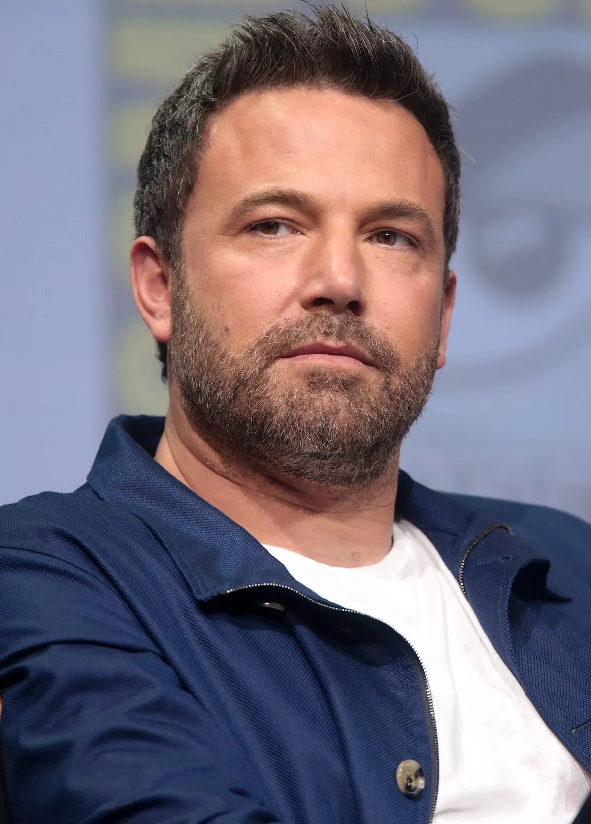 Ben Affleck berjaket biru tua dan kaus putih duduk di panel San Diego Comic-Con 2017, menatap ke samping kamera