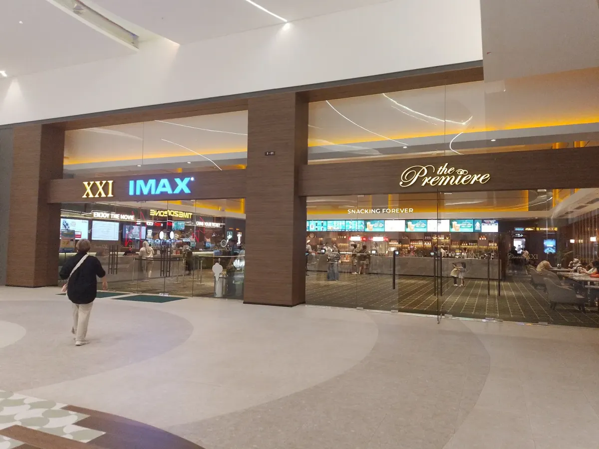 Pintu masuk bioskop dengan papan nama XXI, IMAX, dan the Premiere berdampingan di dalam sebuah mal, dengan konter makanan yang terlihat dari balik kaca