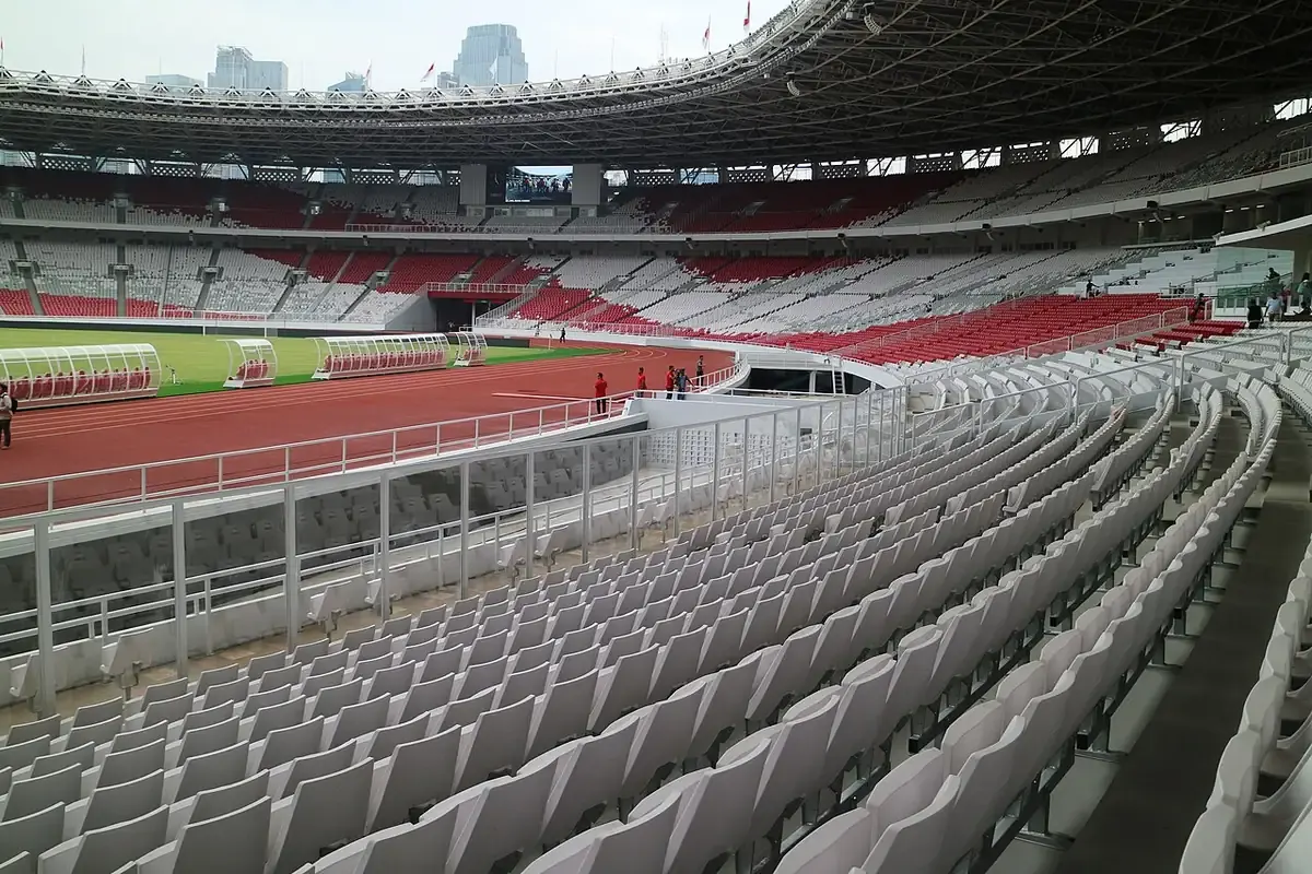 Deretan kursi tribun bawah berwarna putih dan merah di Stadion Utama Gelora Bung Karno setelah renovasi, dengan lintasan atletik dan lapangan di sisi kiri