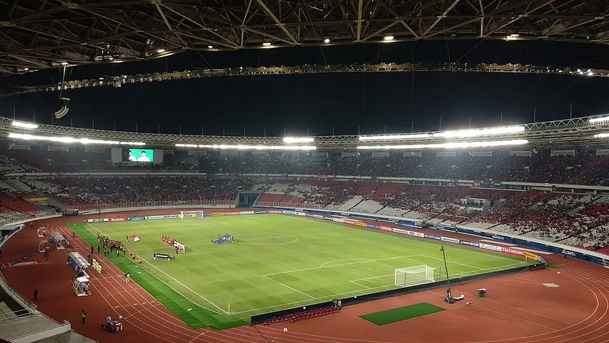 Stadion Utama Gelora Bung Karno pada malam hari dengan lampu stadion menyala, tribun merah putih terisi penonton, dan lapangan hijau dikelilingi lintasan atletik