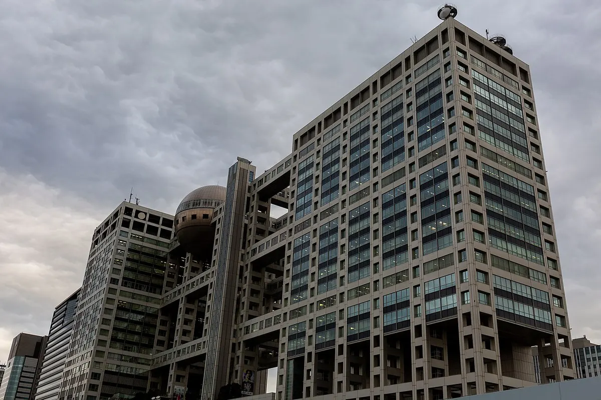 Gedung Fuji Television di Odaiba, Tokyo, dengan bola observasi berwarna perunggu di antara dua menara berangka kisi, di bawah langit mendung