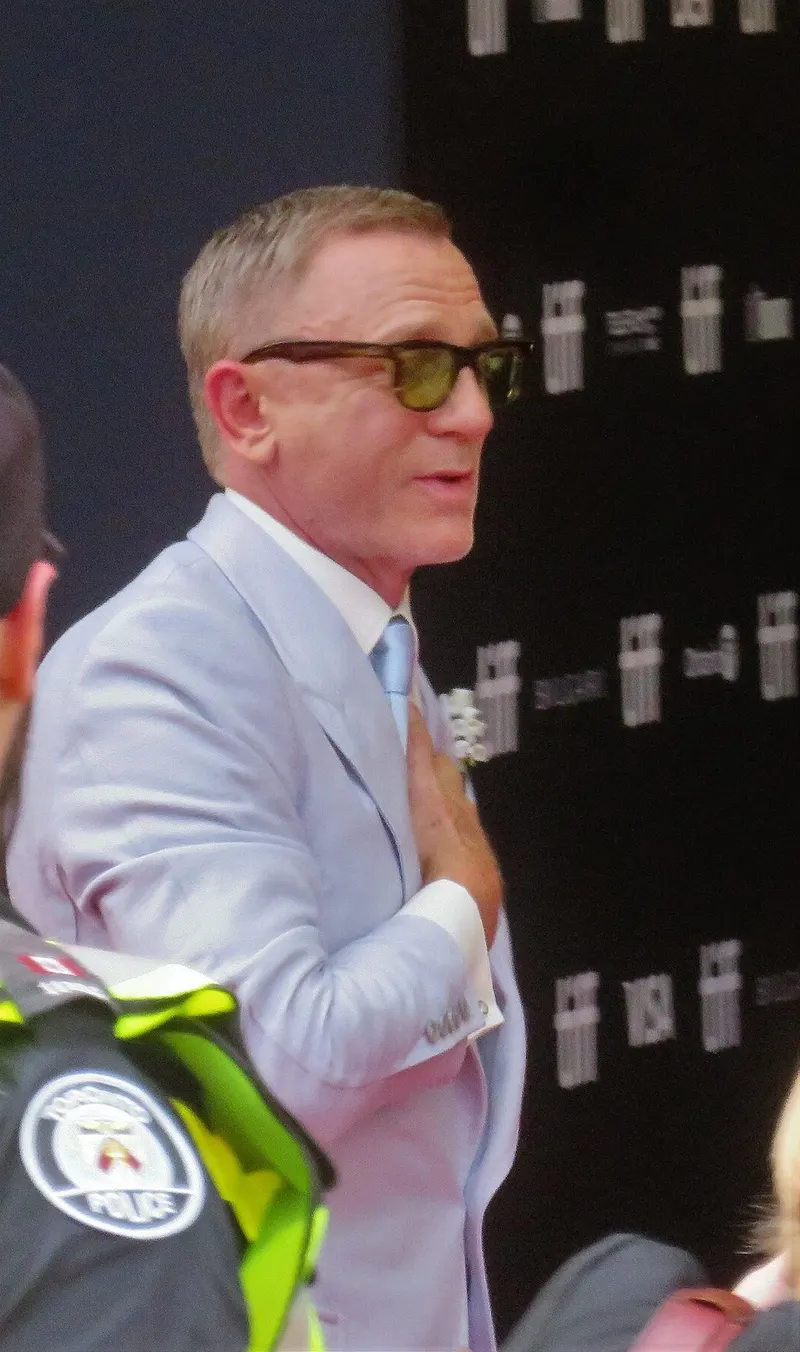 Daniel Craig berjas biru muda dan berkacamata hitam menyapa penonton di karpet merah pemutaran perdana Glass Onion di Toronto