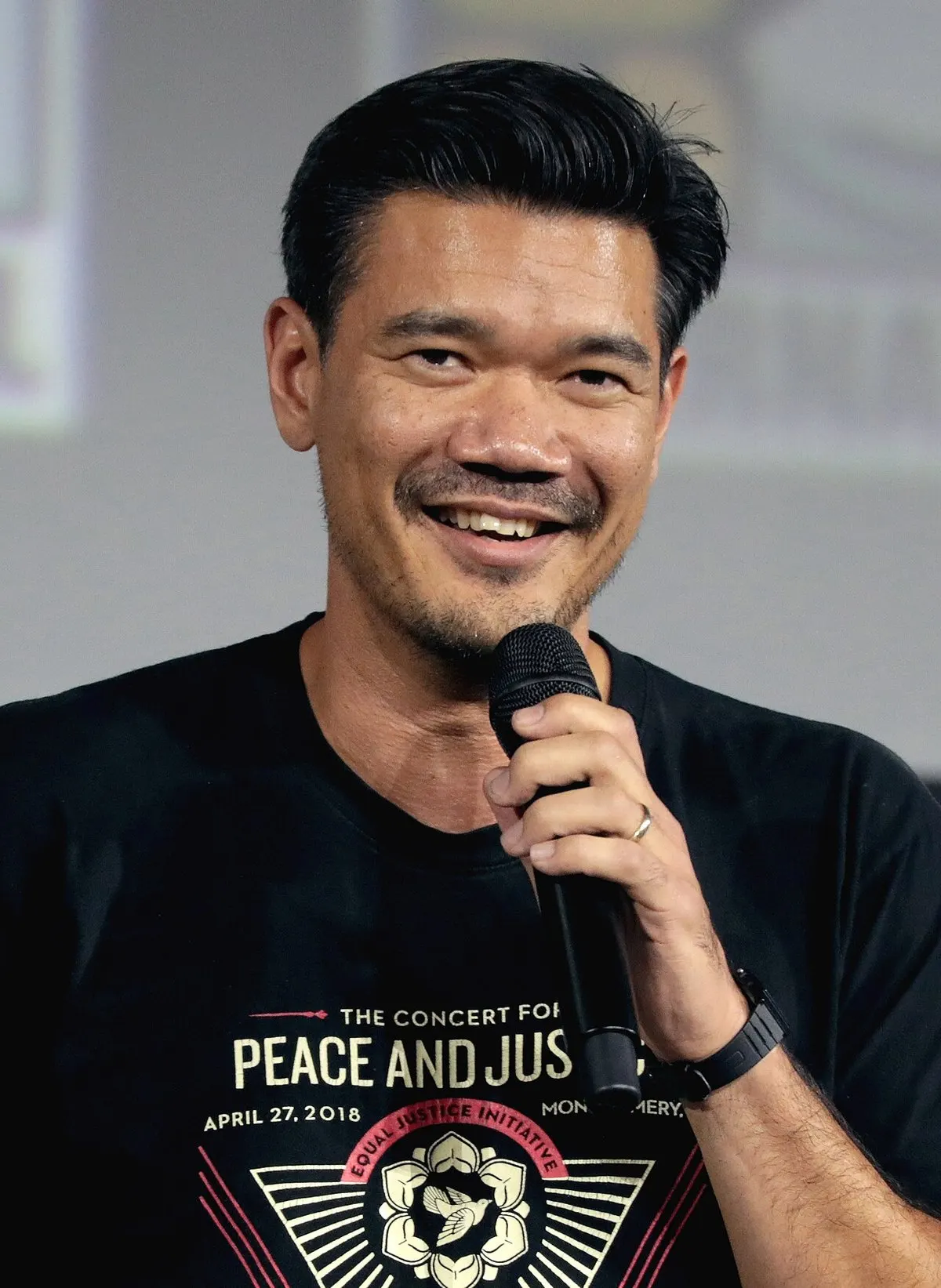 Destin Daniel Cretton berkaus hitam tersenyum sambil memegang mikrofon di panggung San Diego Comic-Con 2019