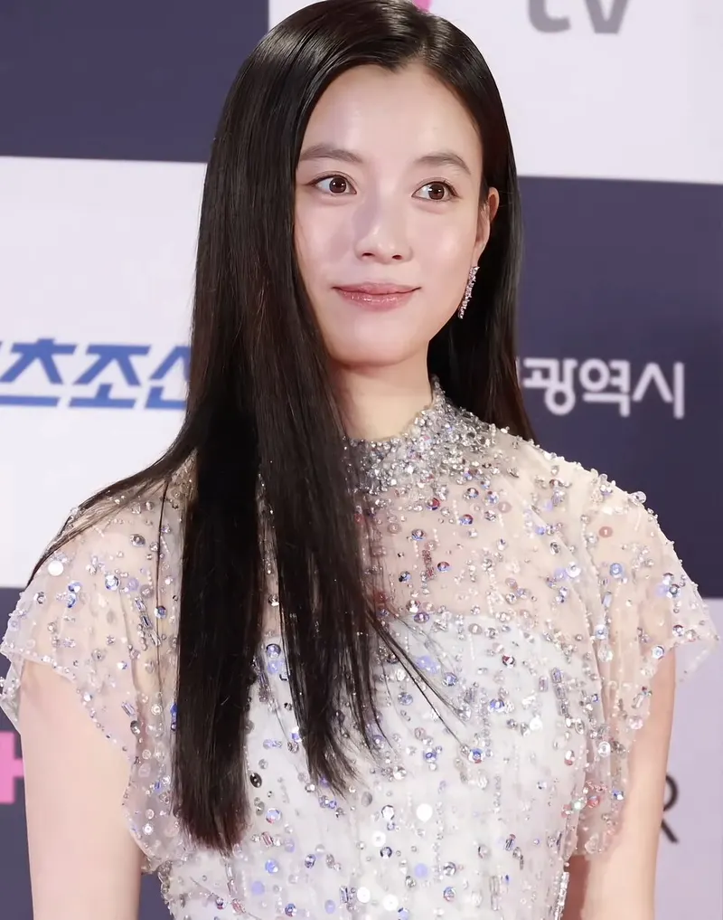Han Hyo-joo berambut panjang lurus dan bergaun berpayet di depan papan acara bertuliskan huruf Korea
