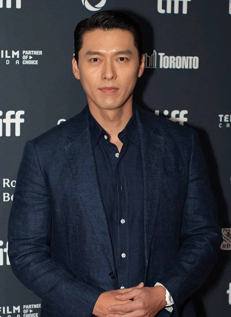 Hyun Bin berjas biru tua berdiri di depan papan bertuliskan tiff dan Toronto