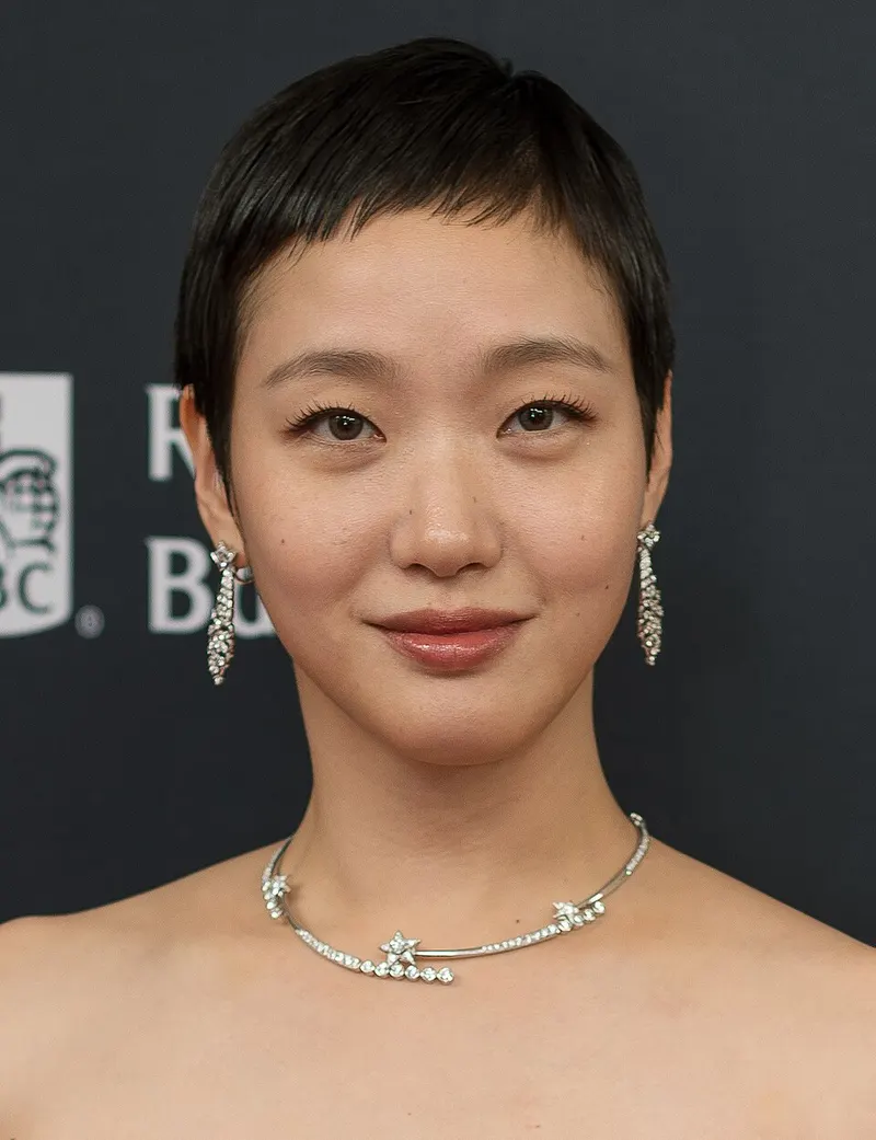 Kim Go-eun berambut sangat pendek dengan anting dan kalung berkilau di depan latar gelap