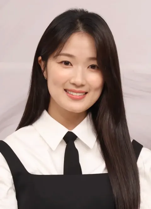 Kim Hye-yoon berambut panjang, berkemeja putih dan berdasi hitam tersenyum