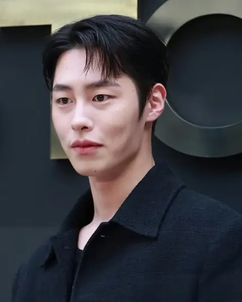 Lee Jae-wook berjaket hitam bertekstur berdiri di depan dinding gelap