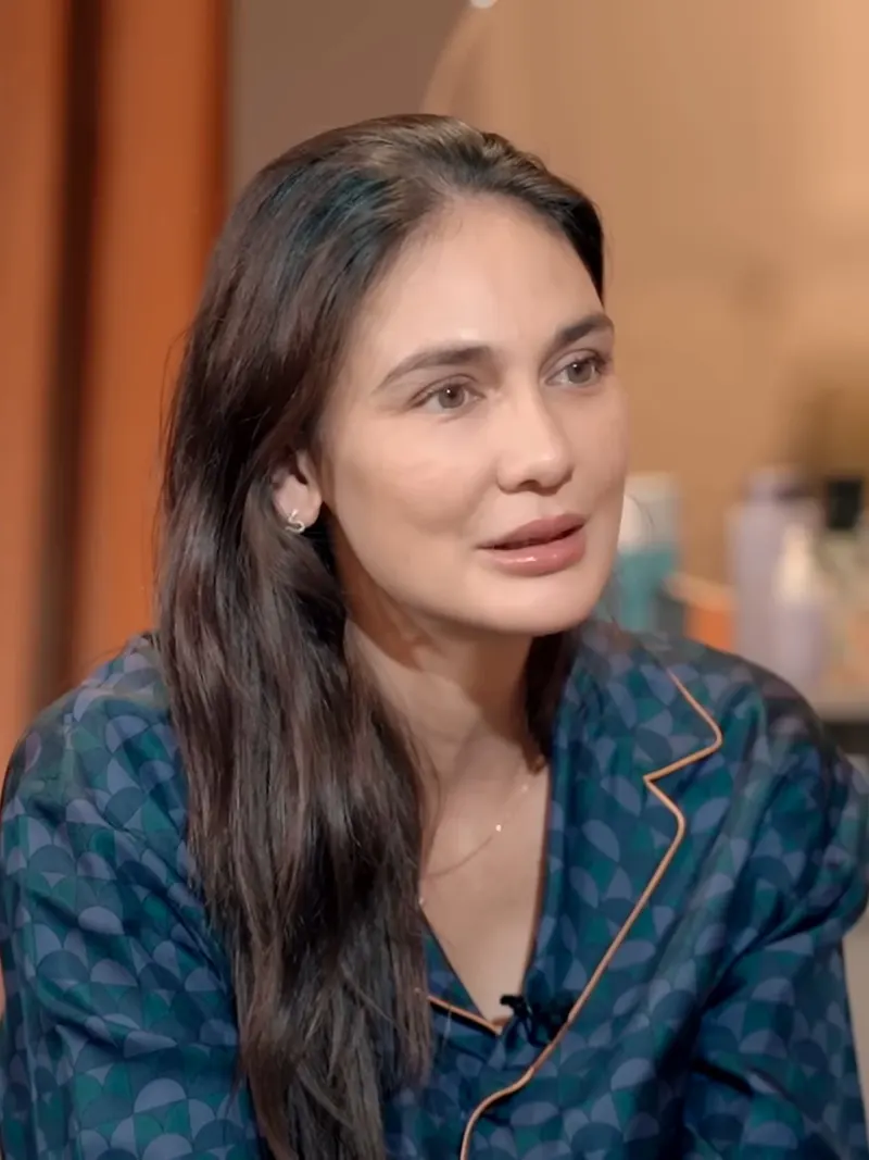 Luna Maya berambut panjang dan berbaju motif biru hijau sedang berbicara dalam wawancara