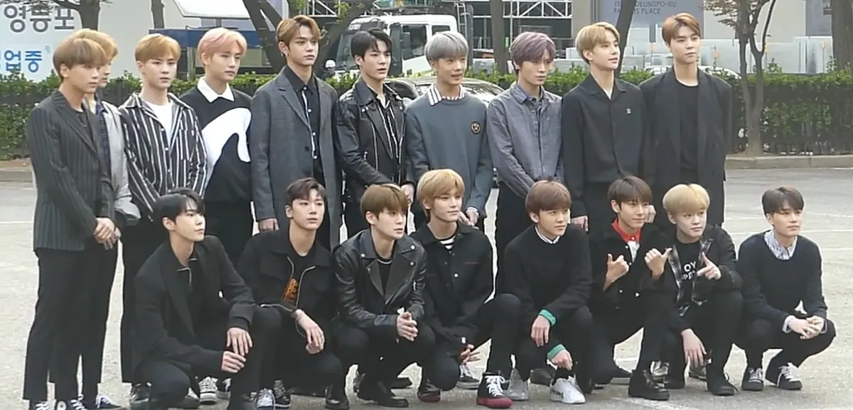 Anggota NCT berpose bersama dalam dua baris di luar gedung sebelum rekaman acara musik