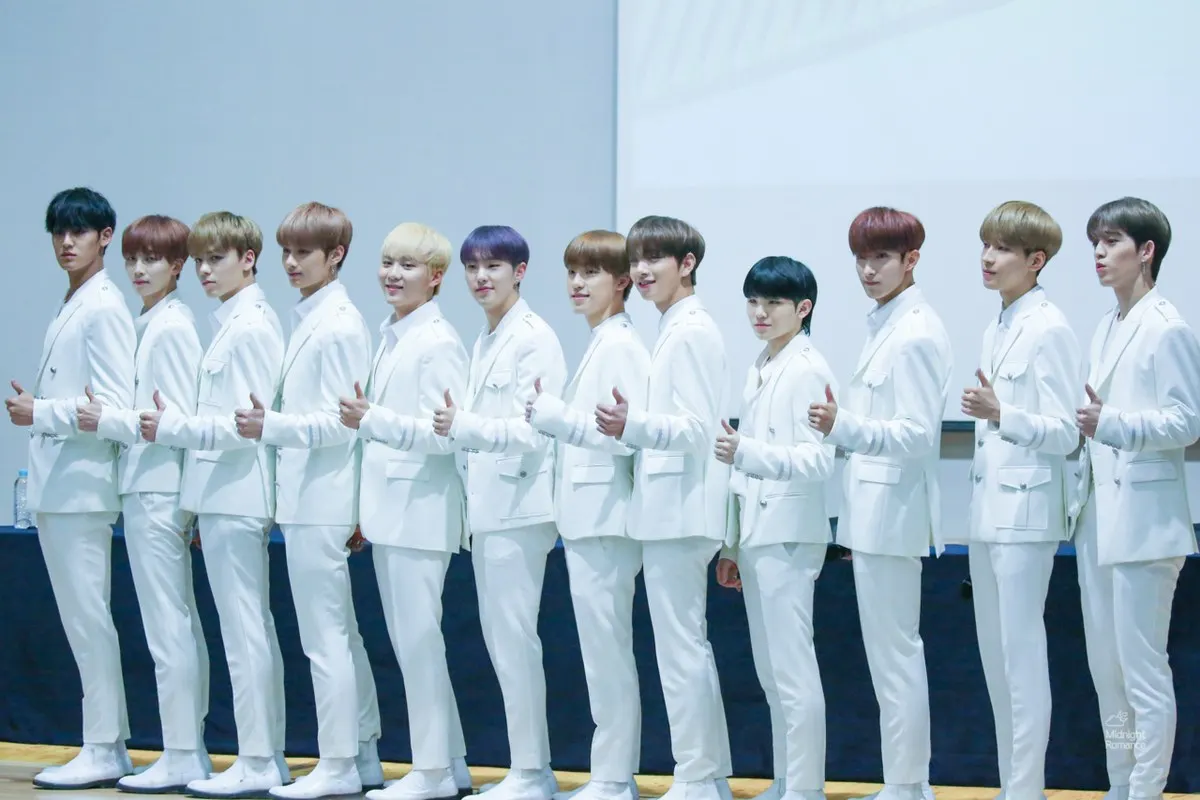 Anggota SEVENTEEN berbaris dengan setelan putih sambil mengacungkan jempol di acara penggemar