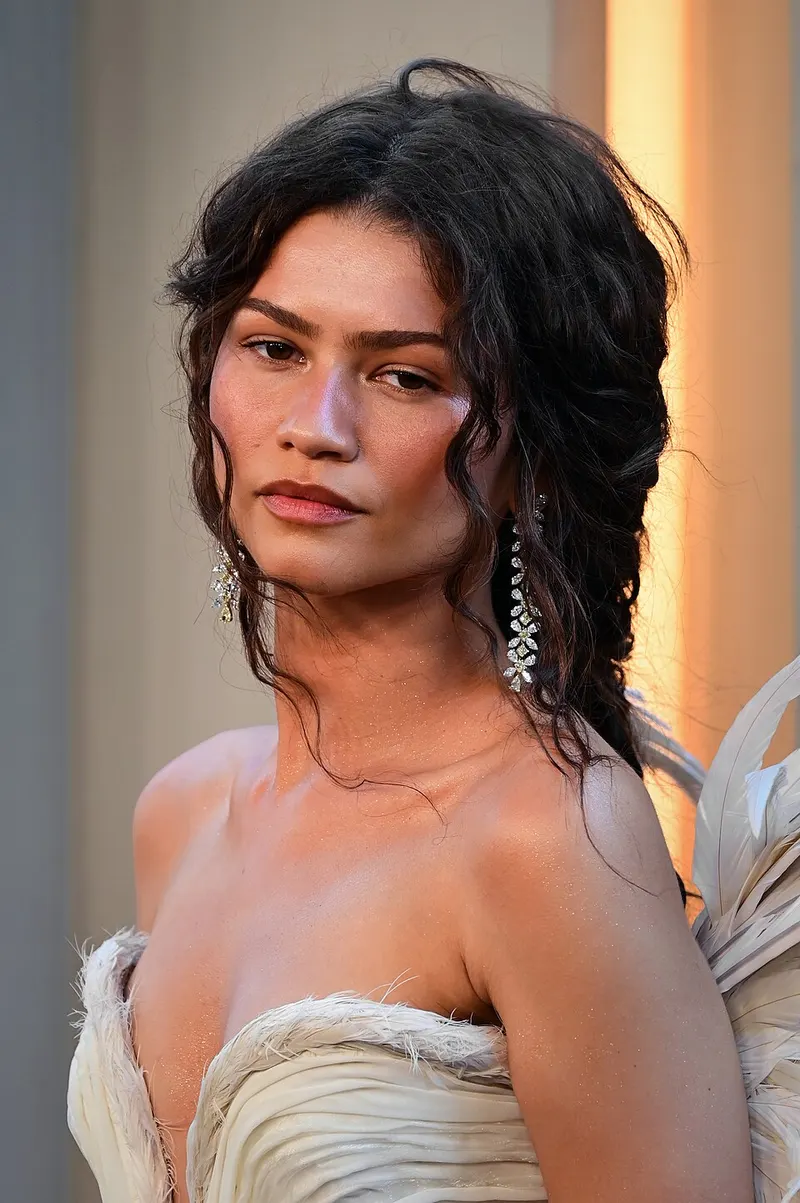 Zendaya berambut ikal gelap dan bergaun putih berbulu di sebuah acara